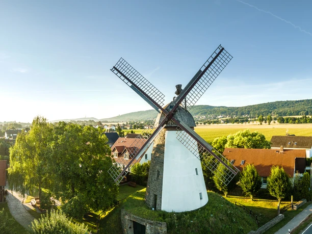 Minden-Windmühle Dützen-Teutoburger-Wald-Tourismus-D-Ketz-003.jpg Historische Windmühle in grüner Landschaft bei blauem Himmel, umgeben von traditionellen Häusern.