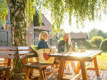Minden-Windmühle Dützen-Teutoburger-Wald-Tourismus-D-Ketz-008.jpg Zwei Frauen sitzen an einem Holztisch unter einem Baum und genießen eine sonnige Gartenidylle.