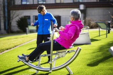 sabrinity_REHAdriburg173.jpg Zwei Frauen üben in sportlicher Kleidung auf einem Outdoor-Fitnessgerät auf einer Rasenfläche.
