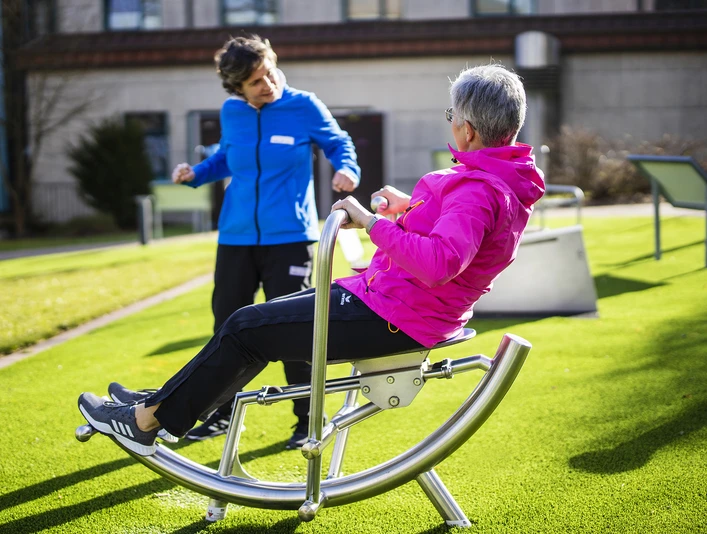 sabrinity_REHAdriburg173.jpg Zwei Frauen üben in sportlicher Kleidung auf einem Outdoor-Fitnessgerät auf einer Rasenfläche.
