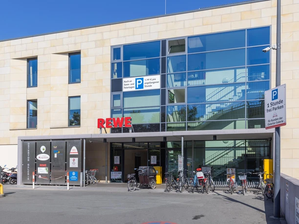 REWE-Eingang in der Ostertor Galerie mit Glasfassade, Fahrrädern und Parkhinweis