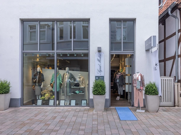 Schaufenster und Eingang von Sigrid Moden mit Damenmode und Pflanzkübeln