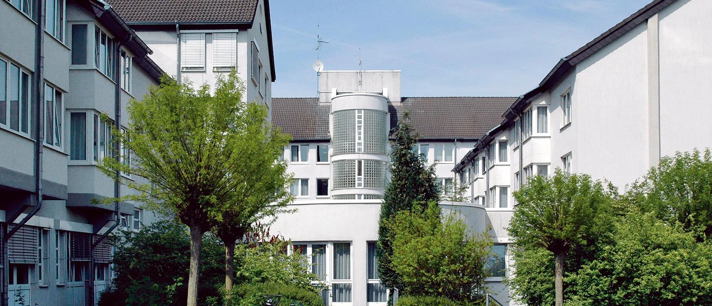 Innenhof der MEDIAN Klinik Flachsheide mit hellen Gebäuden, Bäumen und Sitzbank