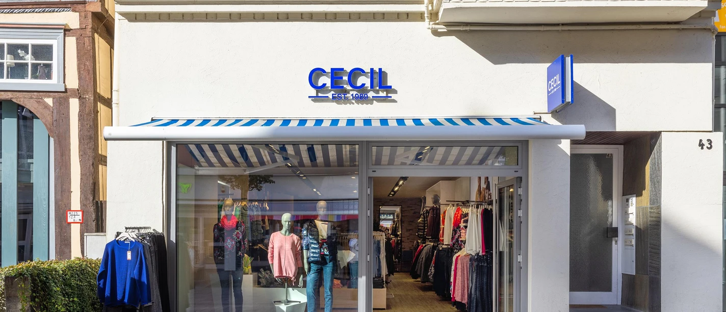 Cecil-Modegeschäft mit Schaufenster, Markise und Kleidung vor heller Fassade