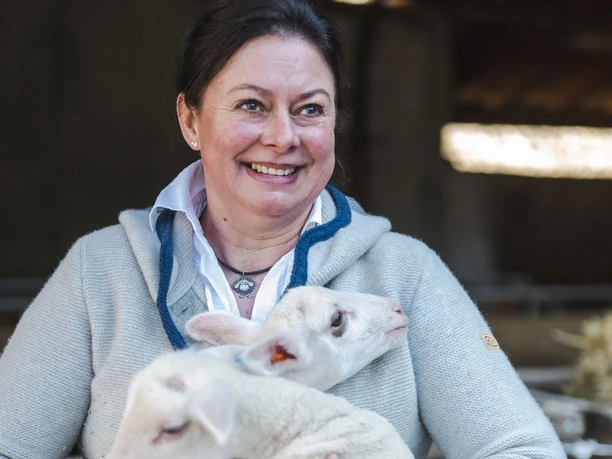 Hofladen Schweb Eine Frau lächelt, während sie zwei weiße Lämmer in den Armen hält.