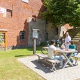 Nieheim-Oeynhausen-Backhaus-Teutoburger-Wald-Tourismus-A-Röser-100.jpg Drei Personen sitzen an einem Picknicktisch vor einem historischen Backstein- und Bruchsteingebäude.