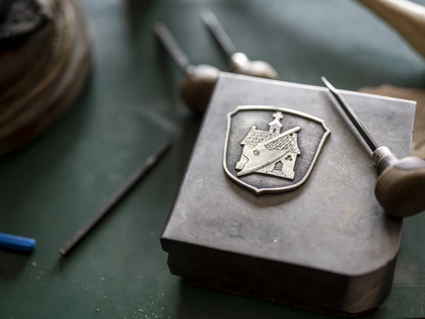 Der Graveur Kaufmann Gravierte Metallplatte mit Wappen und Graveurwerkzeugen auf einer Werkbank.
