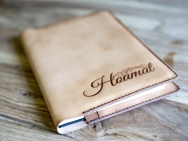 Handwerk & Design Bauer Notizbuch mit Lederumschlag, graviertem Schriftzug "Hoamat", auf Holztisch.