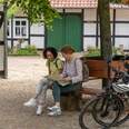 Hille-Kurpark-Rothenuffeln-Teutoburger-Wald-Tourismus-Patrick-Gawandtka-050.jpg Zwei Frauen sitzen auf einer Bank vor einem Fachwerkhaus, umgeben von Bäumen und Fahrrädern.