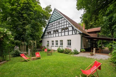 Huellhorst-CafeWaldkristall-Teutoburger-Wald-Tourismus-Patrick-Gawandtka-086-CC-BY-SA.jpg Fachwerkhaus im Grünen mit Liegestühlen im Vordergrund, umgeben von Bäumen und einer Terrasse.
