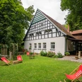 Huellhorst-CafeWaldkristall-Teutoburger-Wald-Tourismus-Patrick-Gawandtka-086-CC-BY-SA.jpg Fachwerkhaus im Grünen mit Liegestühlen im Vordergrund, umgeben von Bäumen und einer Terrasse.