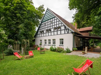 Huellhorst-CafeWaldkristall-Teutoburger-Wald-Tourismus-Patrick-Gawandtka-086-CC-BY-SA.jpg Fachwerkhaus im Grünen mit Liegestühlen im Vordergrund, umgeben von Bäumen und einer Terrasse.