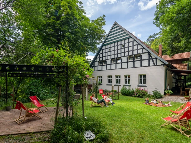Ein idyllisches Fachwerkhaus mit Satteldach inmitten grüner Natur, umgeben von Sitzgelegenheiten.
