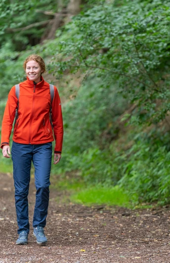 Zwei Frauen wandern lächelnd auf einem Waldweg, umgeben von üppigem grünen Laub.