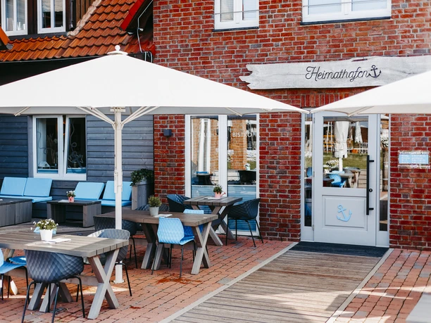 Outdoor area of a maritime-style restaurant with wooden tables, blue chairs and parasols.