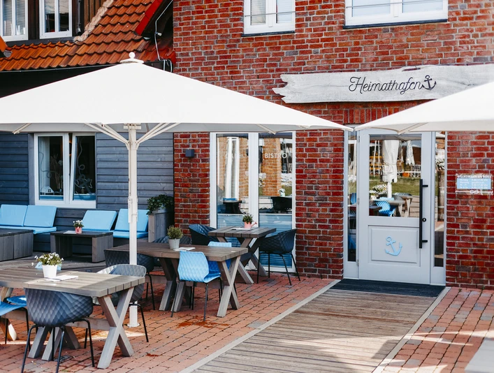 Außenbereich eines Restaurants im maritimen Stil mit Holztischen, blauen Stühlen und Sonnenschirmen.