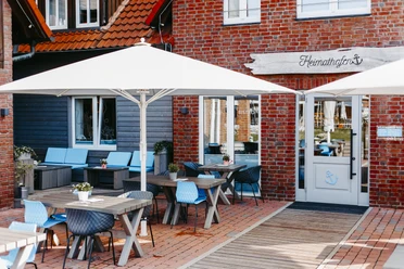 Heimathafen Außenbereich eines Restaurants im maritimen Stil mit Holztischen, blauen Stühlen und Sonnenschirmen.