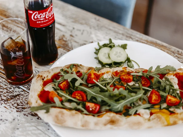 Heimathafen Frische Pizza mit Rucola und Kirschtomaten, dazu Cola im Glas, appetitlich serviert.