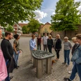 Luebbecke-Stadtfuehrung-Teutoburger-Wald-Tourismus-Patrick-Gawandtka-105.jpg Menschen stehen um ein taktiles Modell einer historischen Stadt versammelt, umgeben von Bäumen und Gebäuden.