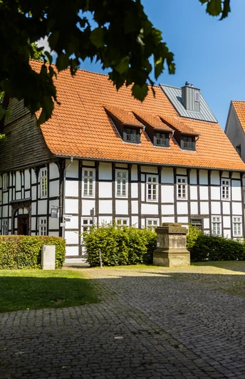 Enger-Widukind-Museum-Teutoburger-Wald-Tourismus-H-Tornow-002-CC-BY-SA.JPG Fachwerkhaus an einem sonnigen Tag, umgeben von gepflastertem Weg und einigen Bäumen im Vordergrund.