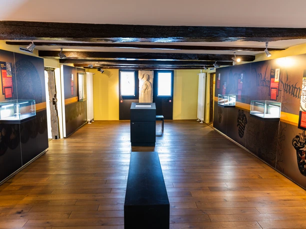 Museumsausstellung mit Holzboden, beleuchteten Vitrinen und Infotafeln an den Wänden.