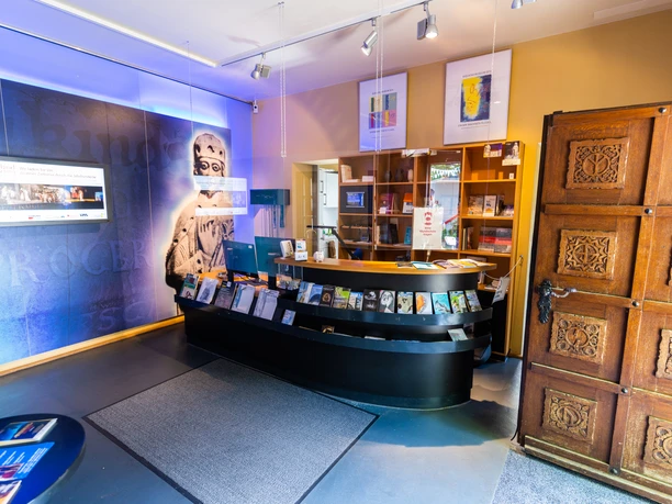 Ein einladender Eingangsbereich eines Museums mit Empfangstresen, Bücherregalen und kunstvollem Holztor.