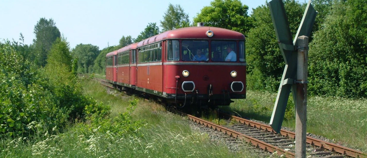 Roter Triebwagen fährt auf einem Bahngleis durch eine grüne Landschaft unter klarem Himmel.