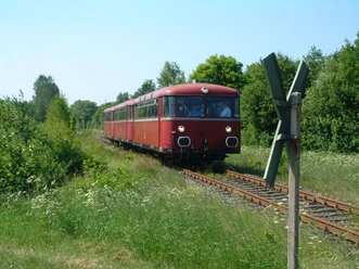 Museumsbahn Roter Triebwagen fährt auf einem Bahngleis durch eine grüne Landschaft unter klarem Himmel.