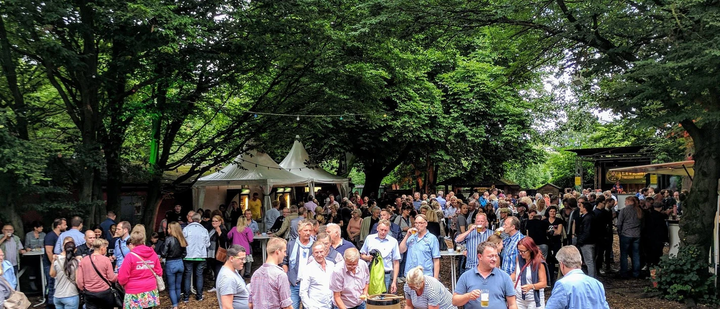 Büdchen am Westerberg .jpg Eine Menschenmenge genießt an einem sonnigen Tag ein geselliges Event im Freien, umgeben von Bäumen.