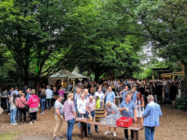 Büdchen am Westerberg .jpg Eine Menschenmenge genießt an einem sonnigen Tag ein geselliges Event im Freien, umgeben von Bäumen.