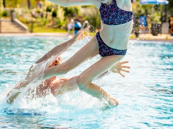 Kirchlengern-Aqua Fun-Teutoburger-Wald-Tourismus-D-Ketz-009.jpg Ein Mädchen in einem gepunkteten Badeanzug springt freudig in ein sonniges Freibad, Wasser spritzt.