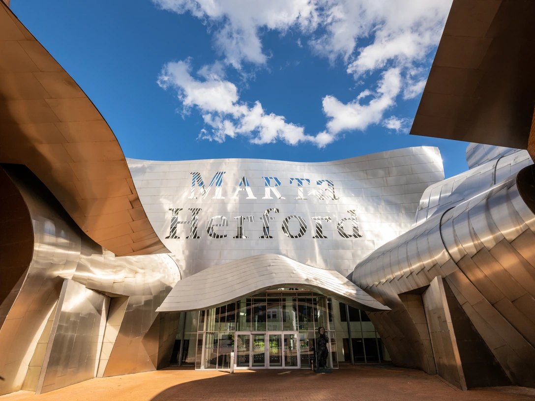 Herford-Marta-Teutoburger-Wald-Tourismus-D-Ketz-098.jpg Gebogenes Gebäude mit glänzender Metallfassade bei blauem Himmel; Schriftzug "Marta Herford".