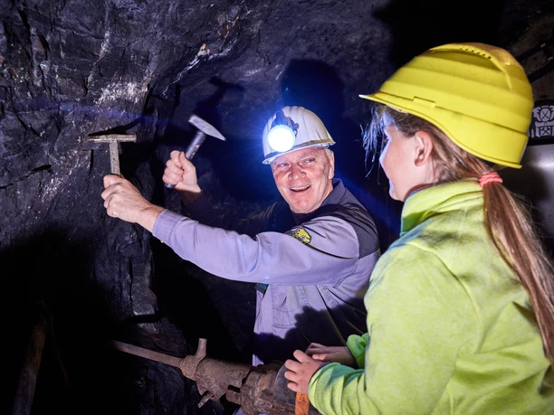 Im Besucherbergwerk Ein Bergmann in Schutzkleidung erklärt einem jungen Besucher gespannt das Arbeiten im Bergwerk.