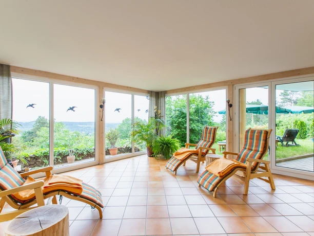 Lichte sauna-relaxruimte met ligstoelen, panoramisch uitzicht op het platteland en toegang tot het terras.