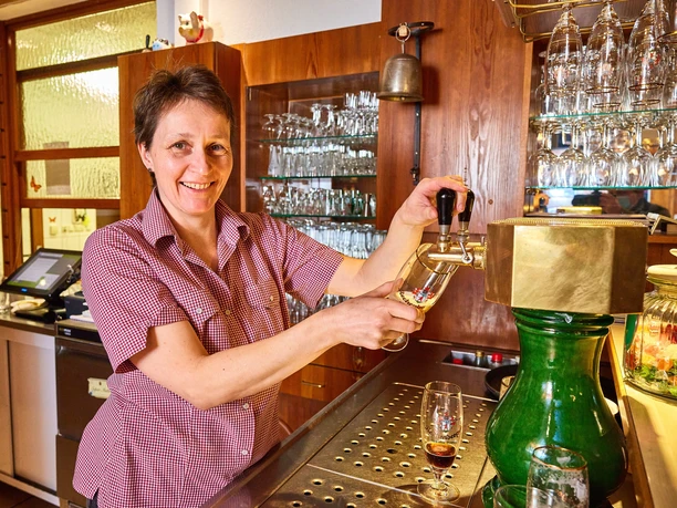 Een vrouw schenkt bier in een rustieke pub, omringd door decoratieve glazen en een tap.