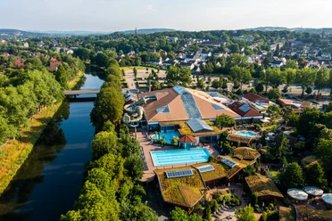Luftbild einer großen Freizeitanlage mit Schwimmbecken, umgeben von Bäumen und einem Fluss.