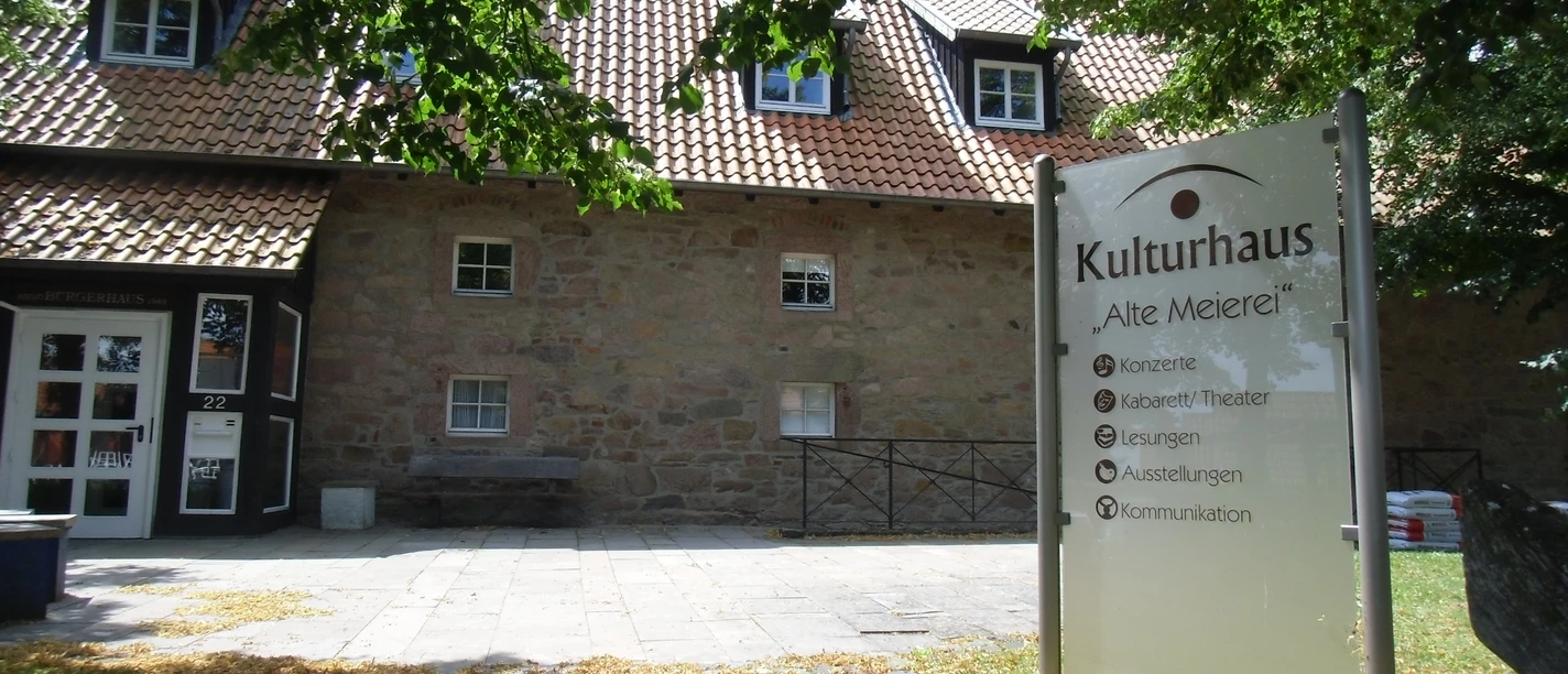 Kulturhaus "Alte Meierei" mit Sandsteinfassade, Schildern für Veranstaltungen und schattigem Eingangsbereich.