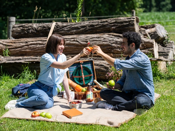 Harsewinkel-Picknick-Teutoburger-Wald-Tourismus-Patrick-Gawandtka-064.jpg Ein Paar genießt ein sommerliches Picknick im Grünen, umgeben von Natur und Holzstämmen.