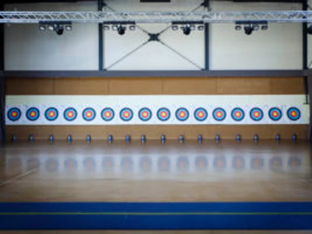 Bogensport Landhaus Nicolai Innenansicht einer Sporthalle mit elf bunten Zielscheiben an der Wand, darunter blaue Kegel auf dem Boden.