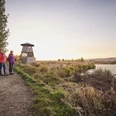 Großes Torfmoor Zwei Frauen wandern bei Sonnenuntergang neben einem ruhigen Flusslauf und einem hölzernen Aussichtsturm.