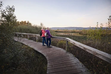Großes Torfmoor-Teutoburger-Wald-Tourismus-M-Rothbrust-005.jpg Zwei Personen spazieren gemeinsam auf einem hölzernen Pfad durch eine herbstliche, bewachsene Landschaft.