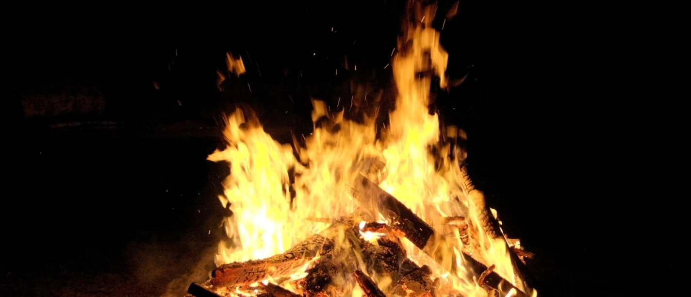Osterfeuer Loderndes Osterfeuer mit brennenden Holzscheiten vor dunklem Hintergrund