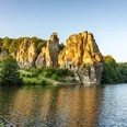 Horn-Bad Meinberg-Externsteine-Teutoburger-Wald-Tourismus-D-Ketz-010-CC-BY-SA.jpg Felsenformation in grüner Landschaft spiegelt sich im See, umgeben von Bäumen bei Sonnenuntergang.