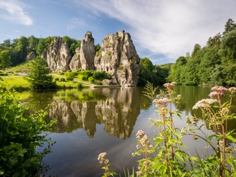 Bizarr geformte Sandsteinfelsen spiegeln sich in einem malerischen See, umgeben von grüner Natur.