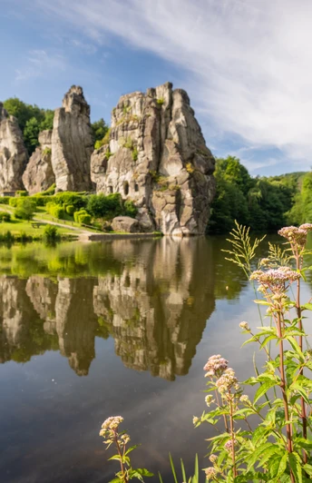 Bizarr geformte Sandsteinfelsen spiegeln sich in einem malerischen See, umgeben von grüner Natur.