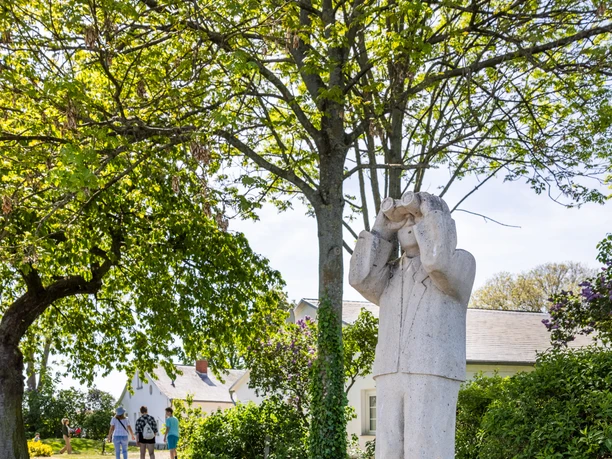Skulptur eines Mannes mit Fernglas auf einem Sockel, umgeben von grünen Bäumen auf der Insel Wilhelmstein.