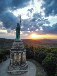 Hermannsdenkmal-Detmold-Teutoburger-Wald-Tourismus-D-Ketz-111-CC-BY-SA.jpg Hermannsdenkmal bei Detmold, eine Statue des Cheruskerfürsten Arminius, umgeben von Wald bei Sonnenuntergang.
