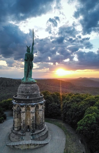 Hermannsdenkmal-Detmold-Teutoburger-Wald-Tourismus-D-Ketz-111-CC-BY-SA.jpg Hermannsdenkmal bei Detmold, eine Statue des Cheruskerfürsten Arminius, umgeben von Wald bei Sonnenuntergang.