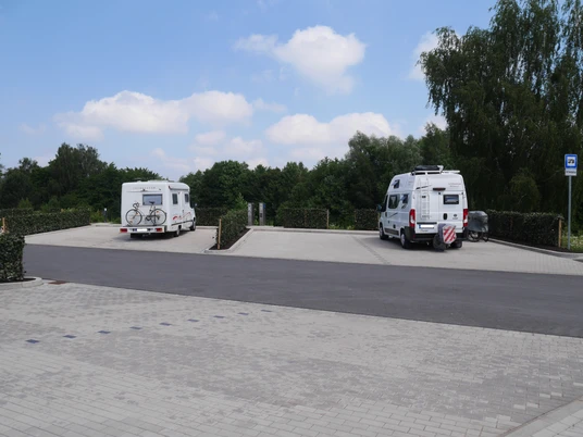 Wohnmobilstellplatz Werrebogen Zwei Wohnmobile parken auf einem gepflasterten Stellplatz, umgeben von grünen Bäumen und Hecken.
