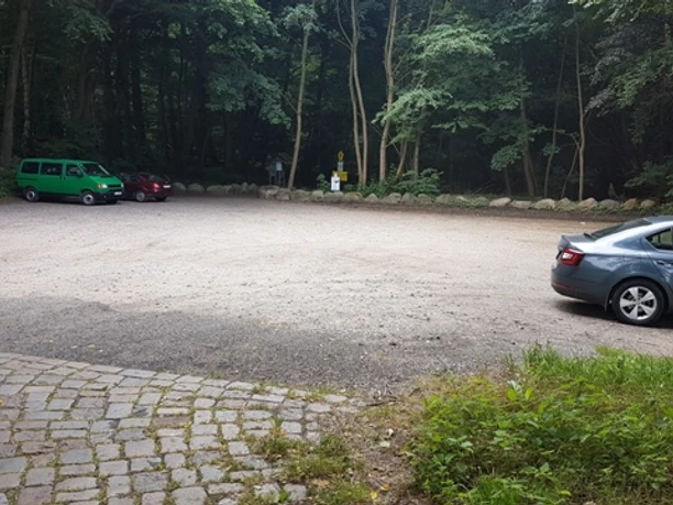 Wanderparkplatz Garrensee Sandparkplatz mit parkenden Autos. Im Hintergrund stehen Bäume